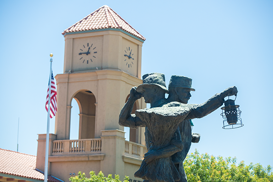 Statue of two figures holding a lantern in front of a clock tower with an American flag